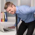 handsome man feeling pain in back. Businessman suffering from back pain at office